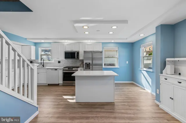 a kitchen with stainless steel appliances granite countertop a stove top oven a sink dishwasher and a refrigerator with wooden floor