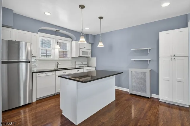 a kitchen with stainless steel appliances granite countertop a sink a stove a refrigerator and island with wooden floor