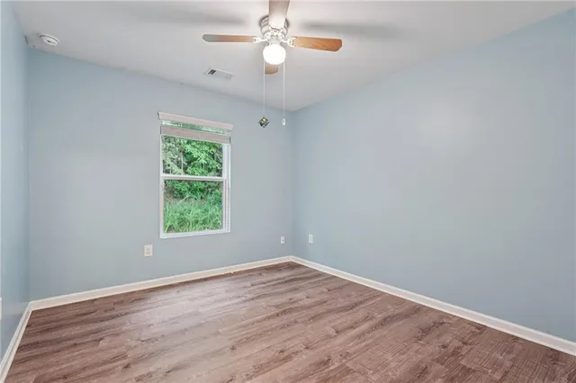 an empty room with wooden floor chandelier fan and windows