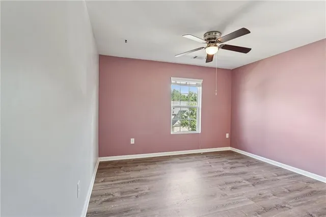 an empty room with wooden floor fan and windows