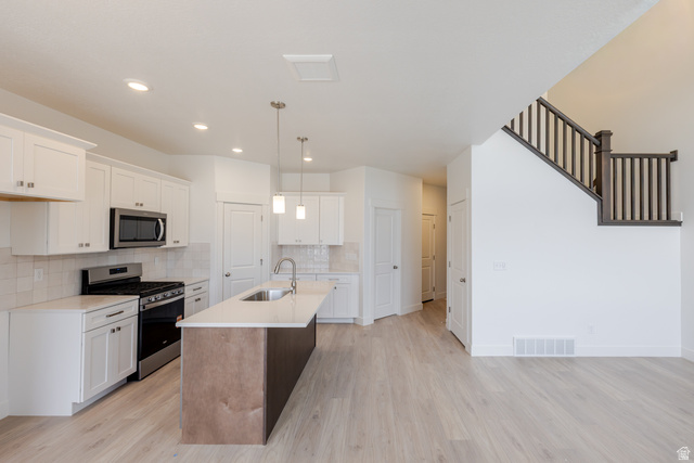 4748 Heartwood Road, Unit 434 Mapleton, UT 84664 - Photo 6 of 18 Kitchen with stainless steel appliances, a kitchen island with sink, light wood finished floors, tasteful backsplash, and light stone countertops