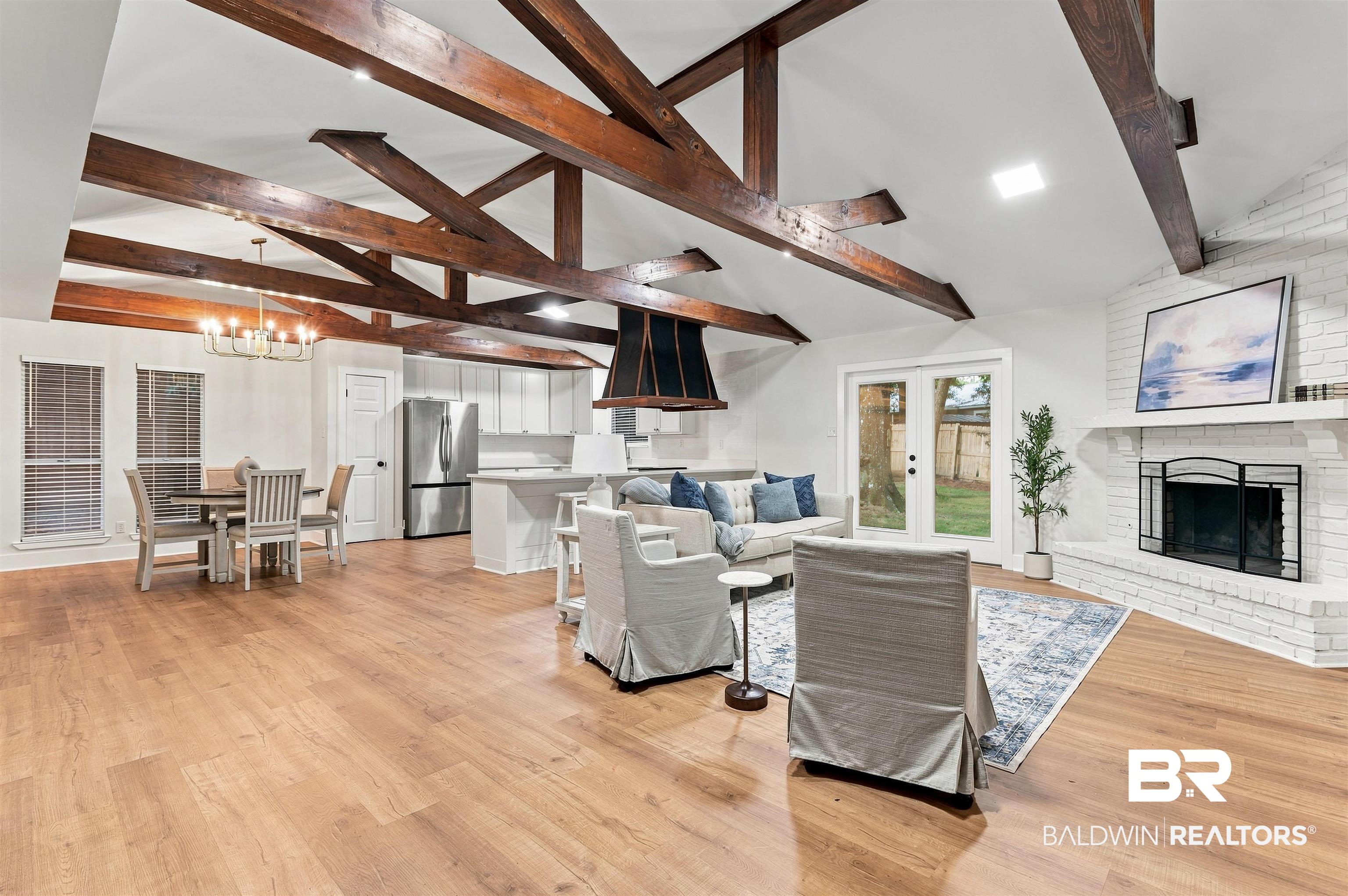 599 Ridgewood Drive Daphne, AL 36526 - Photo 2 of 41 Open-concept living space featuring wood-finish flooring, exposed ceiling beams, a white brick fireplace with mantel, white cabinetry, and stainless steel appliances