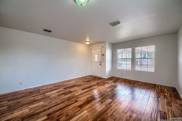a view of an empty room with wooden floor and a window