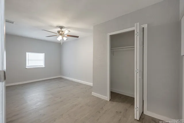 an empty room with wooden floor chandelier fan and windows