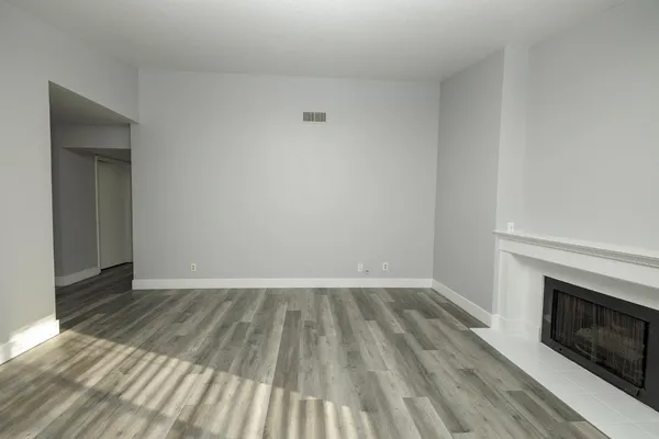 a view of an empty room with wooden floor and a fireplace