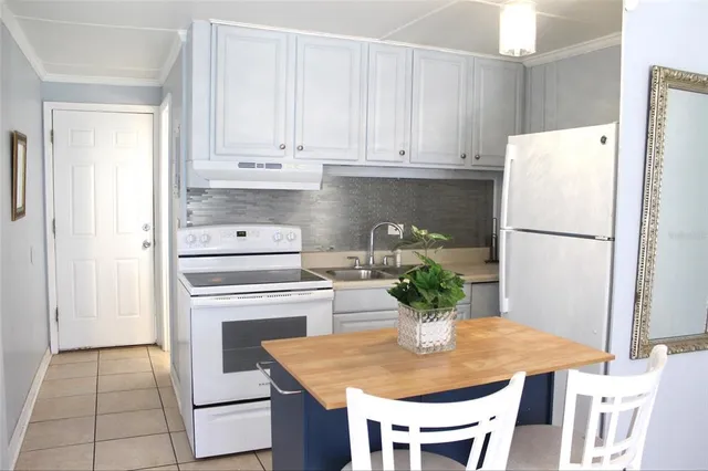 a white kitchen with a stove a refrigerator a dining table and chairs