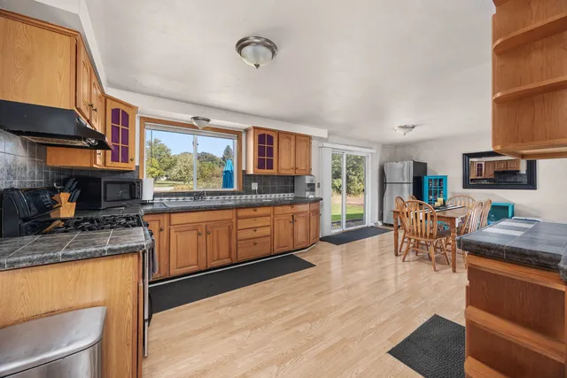 a kitchen with stainless steel appliances granite countertop wooden cabinets a stove a sink and a dining table with wooden floor