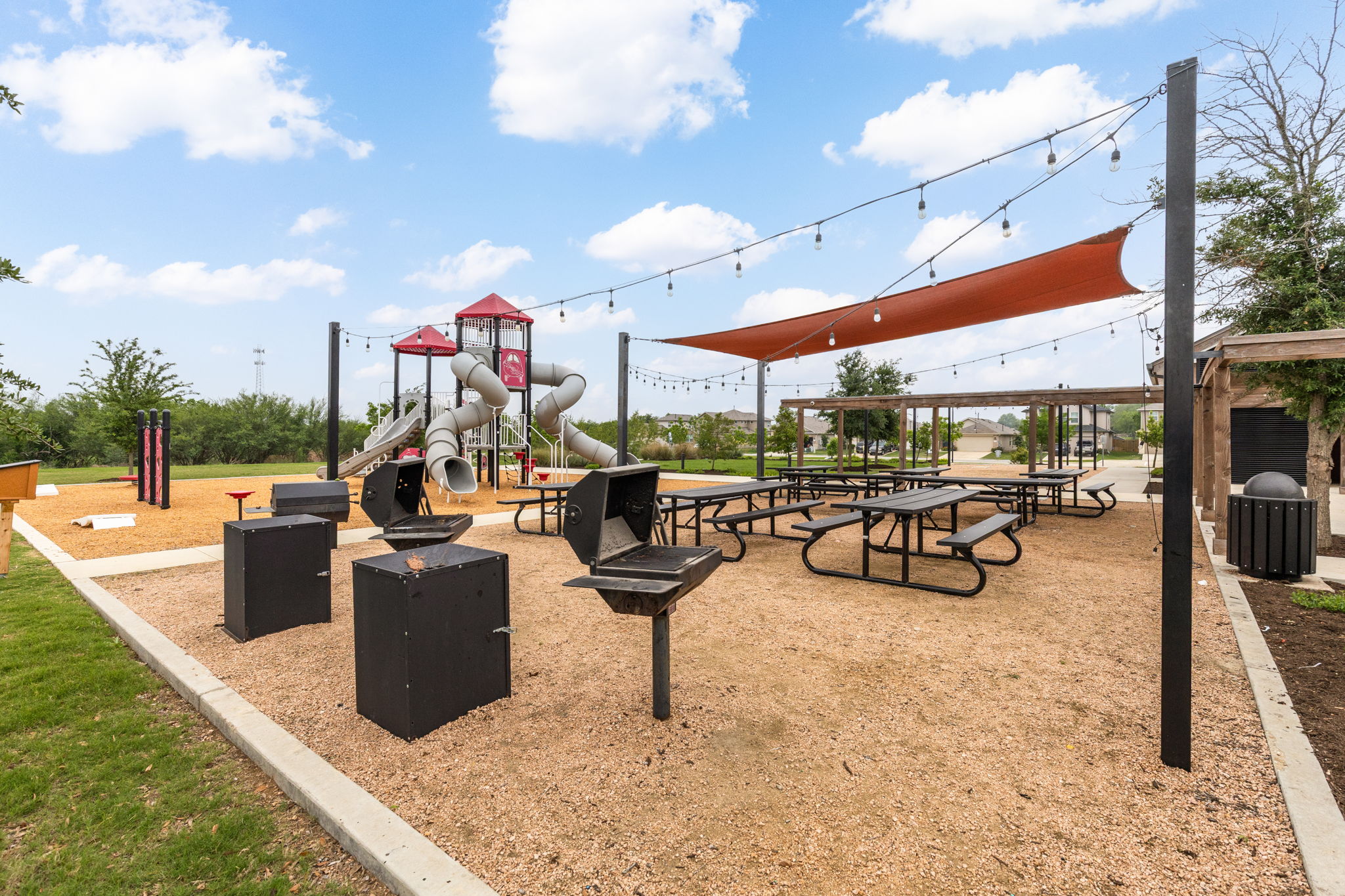 281 Jayden Drive Kyle, TX 78640 - Photo 35 of 36 Community playground featuring multiple slides and structures, a shaded picnic area with string lights, and dedicated grilling stations