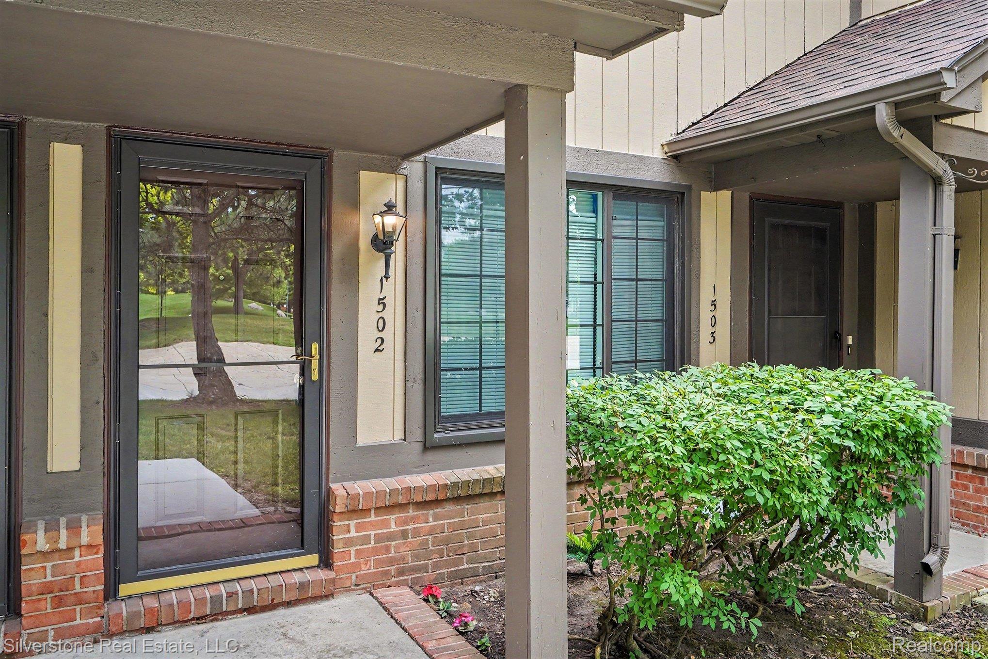 1502 Meadowside Drive Rochester, MI 48307 - Photo 3 of 27 Exterior entry featuring a full-view storm door, brick foundation, and wall-mounted outdoor lighting