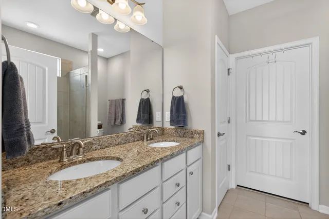 a bathroom with a granite countertop double vanity sink a mirror and a shower