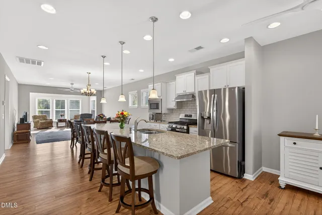 a kitchen with stainless steel appliances granite countertop a kitchen island a stove a refrigerator a kitchen island a dining table and chairs with wooden floor