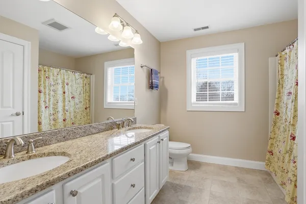 a bathroom with a granite countertop double vanity sink a mirror and a toilet