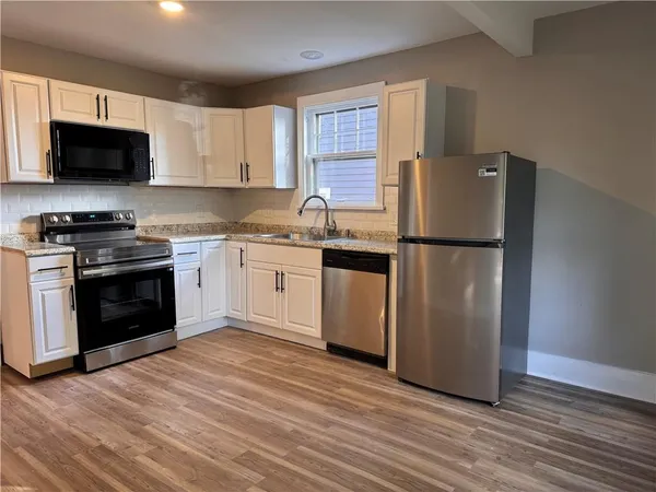 a kitchen with stainless steel appliances granite countertop a stove top oven a refrigerator and a sink with wooden floor