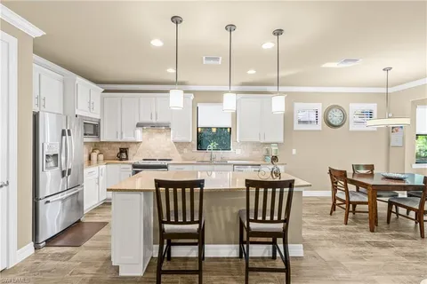 a kitchen with stainless steel appliances granite countertop a stove a refrigerator a kitchen island a dining table and chairs with wooden floor