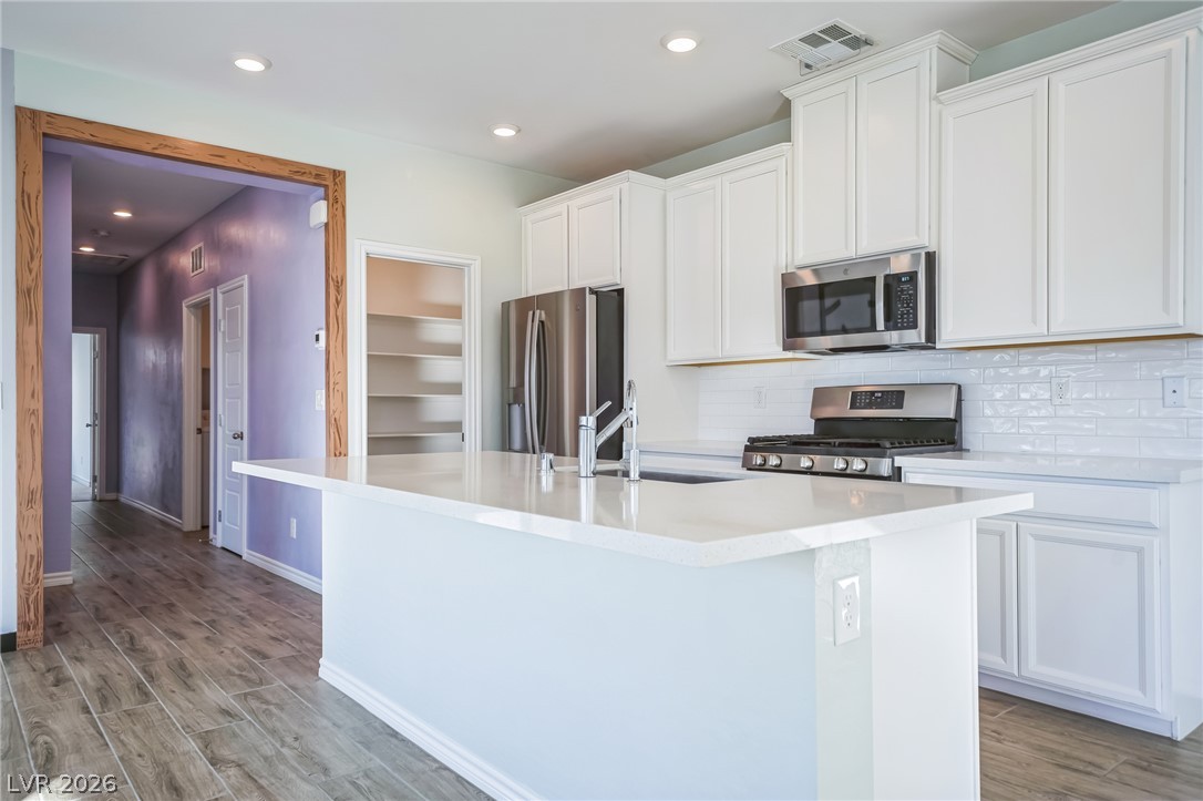 7348 North Decatur Boulevard, Unit 1 North Las Vegas, NV 89084 - Photo 4 of 17 A well-appointed kitchen features a central island, modern appliances, and crisp white cabinetry, seamlessly flowing into a lavender-hued hallway.