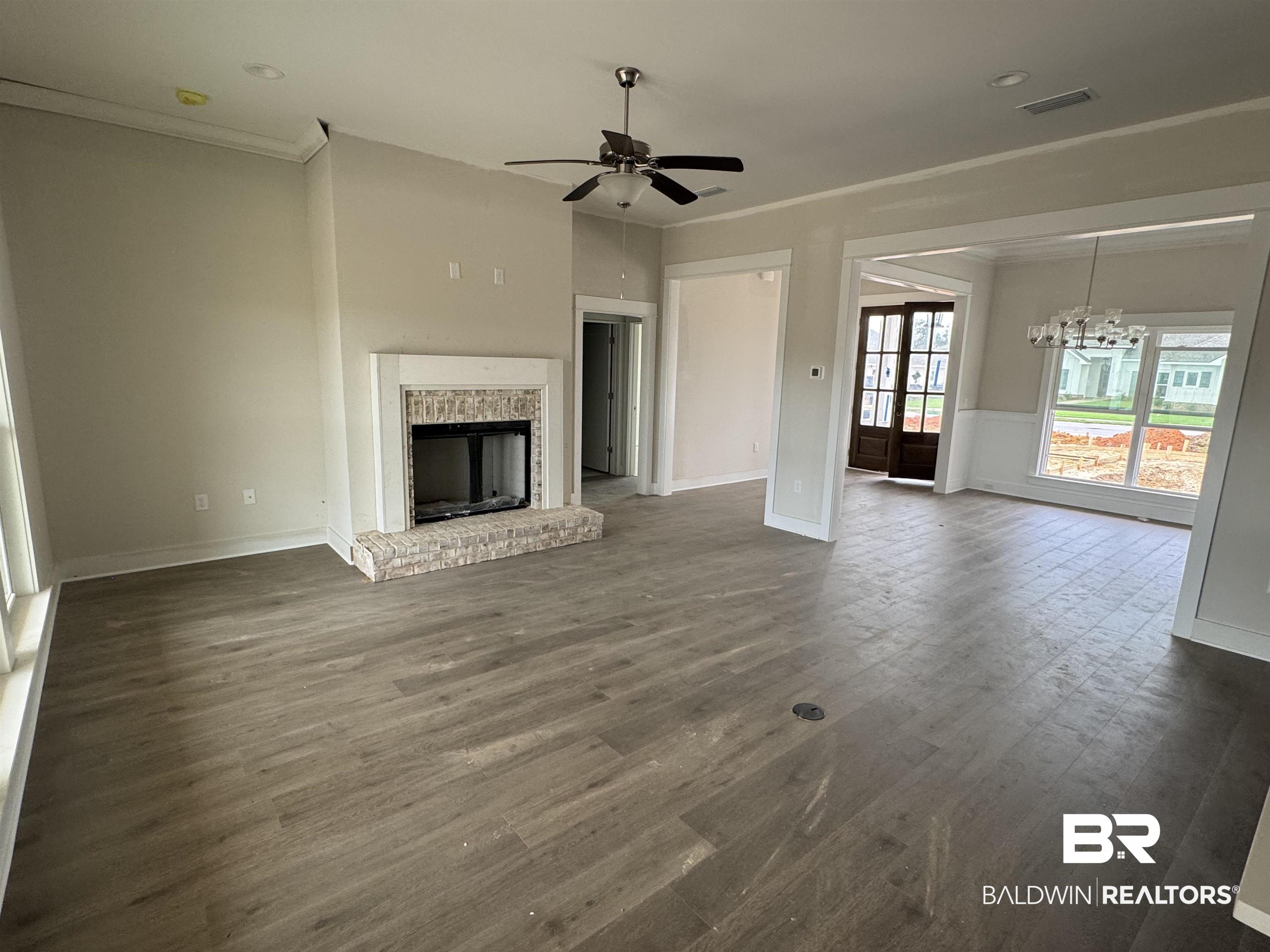 23579 Travis Stock Street Foley, AL 36535 - Photo 9 of 31 Unfurnished living room featuring dark wood-type flooring, a fireplace, ornamental molding, and ceiling fan with notable chandelier