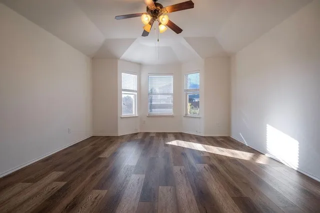 an empty room with wooden floor chandelier fan and windows