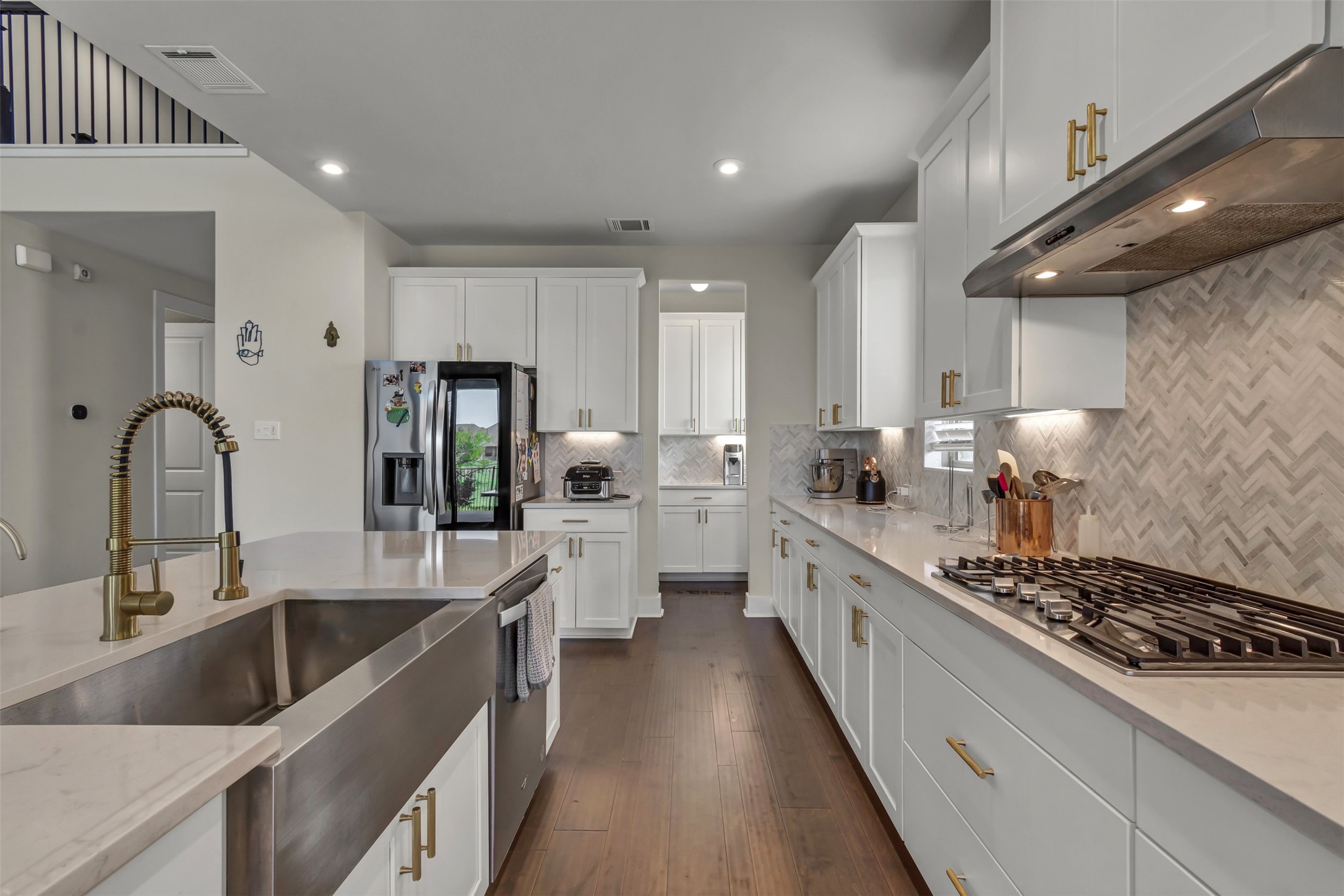 209 Azalea Spg Road Liberty Hill, TX 78642 - Photo 17 of 29 Kitchen featuring white cabinetry with gold-toned hardware, light countertops, wood-finish flooring, and a herringbone-patterned backsplash