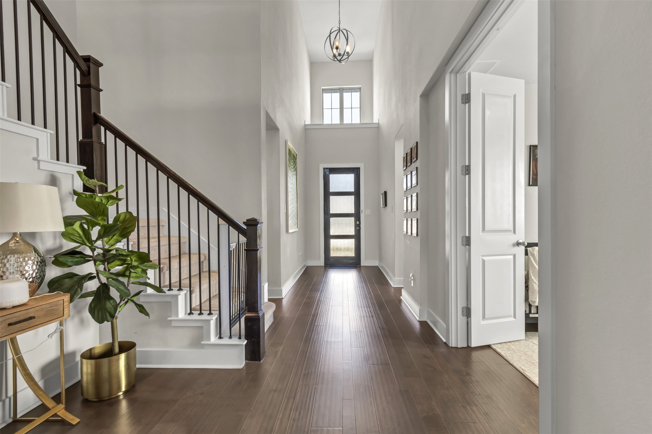 209 Azalea Spg Road Liberty Hill, TX 78642 - Photo 3 of 29 Grand foyer featuring wood-finish flooring, a two-story ceiling, a contemporary black entry door with frosted glass panels, and a staircase with dark wood handrails and black iron balusters