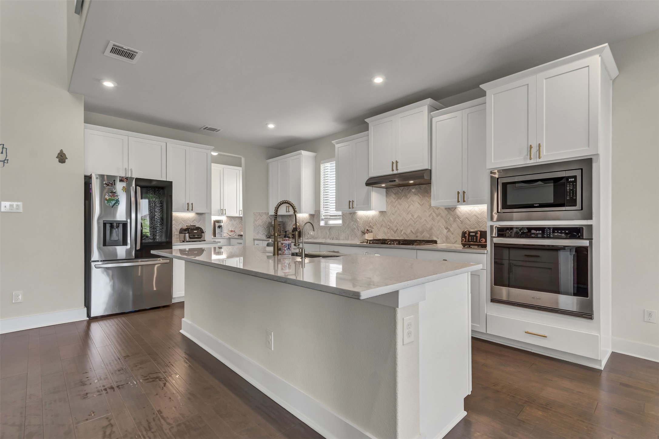 209 Azalea Spg Road Liberty Hill, TX 78642 - Photo 5 of 29 Contemporary kitchen featuring an island with a light-toned countertop, white cabinetry, integrated stainless steel appliances, a herringbone tile backsplash, and dark wood-finish flooring