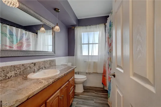a bathroom with a granite countertop sink a mirror a toilet and a window