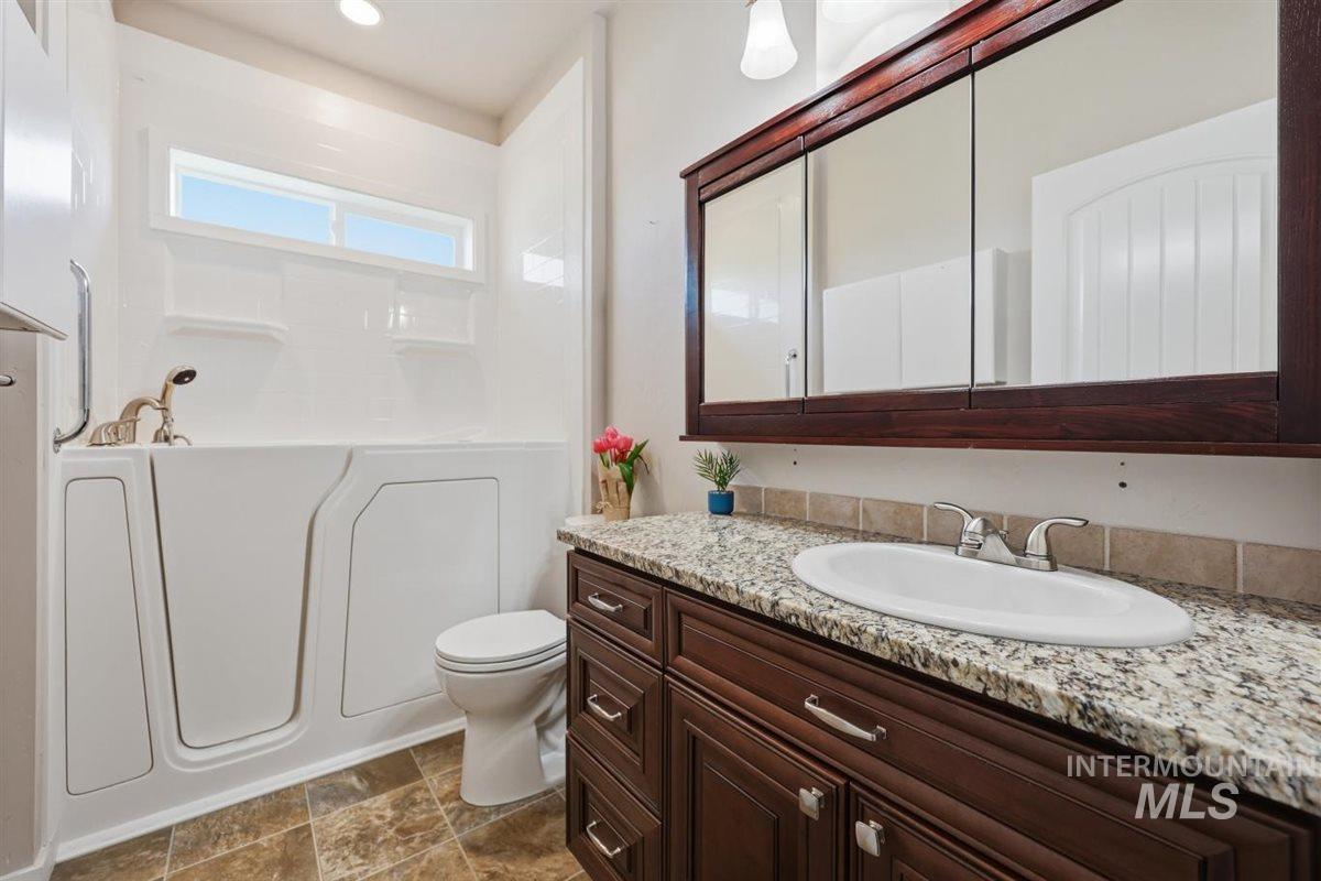13496 Hockberger Ranch Road Caldwell, ID 83607 - Photo 10 of 40 Bathroom featuring a walk-in tub with grab bar, a single vanity with stone-finish countertop, a white oval undermount sink, a dark wood-finish vanity cabinet, and a mirrored medicine cabinet with a dark wood-finish frame