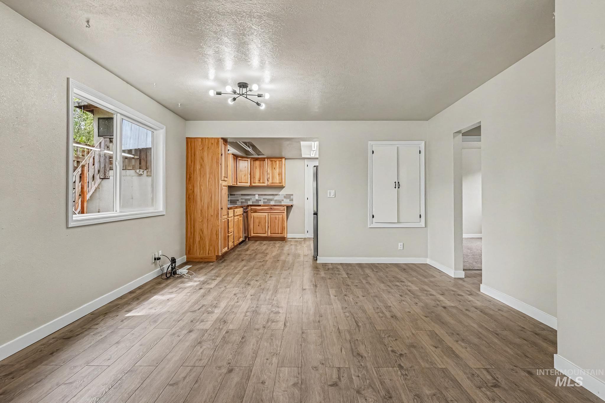 1023 State Street Weiser, ID 83672 - Photo 5 of 25 Open concept living space featuring wood-finish flooring, a modern sputnik-style light fixture, and a kitchen with wood cabinetry and a tiled backsplash