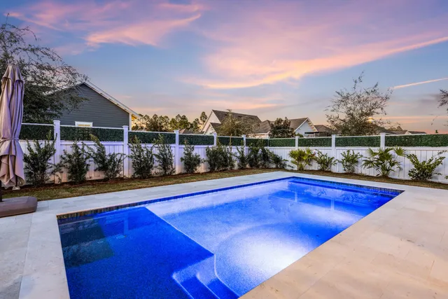 a swimming pool with lawn chairs and large trees