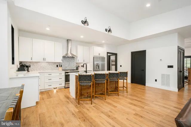 a kitchen with stainless steel appliances kitchen island granite countertop a stove a sink a refrigerator and white cabinets with wooden floor