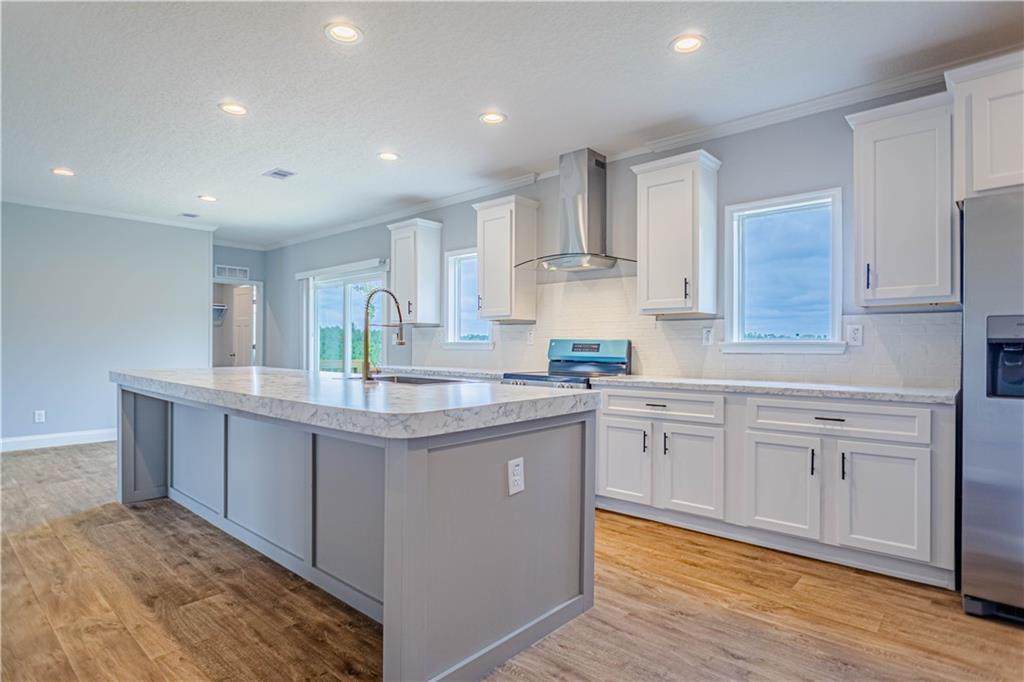 Kitchen featuring a large island with sink, white shaker-style cabinetry, stainless steel appliances, and wood-finish flooring