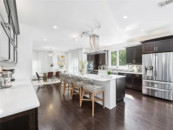 a kitchen with stainless steel appliances kitchen island granite countertop a stove a sink dishwasher a dining table and chairs with wooden floor