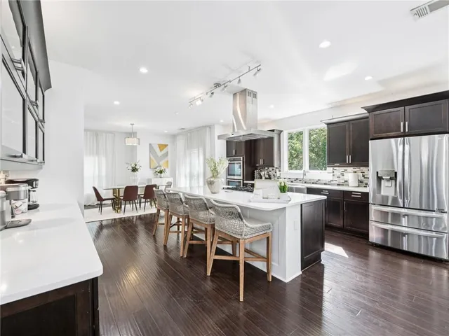 a kitchen with stainless steel appliances kitchen island granite countertop a stove a sink dishwasher a dining table and chairs with wooden floor