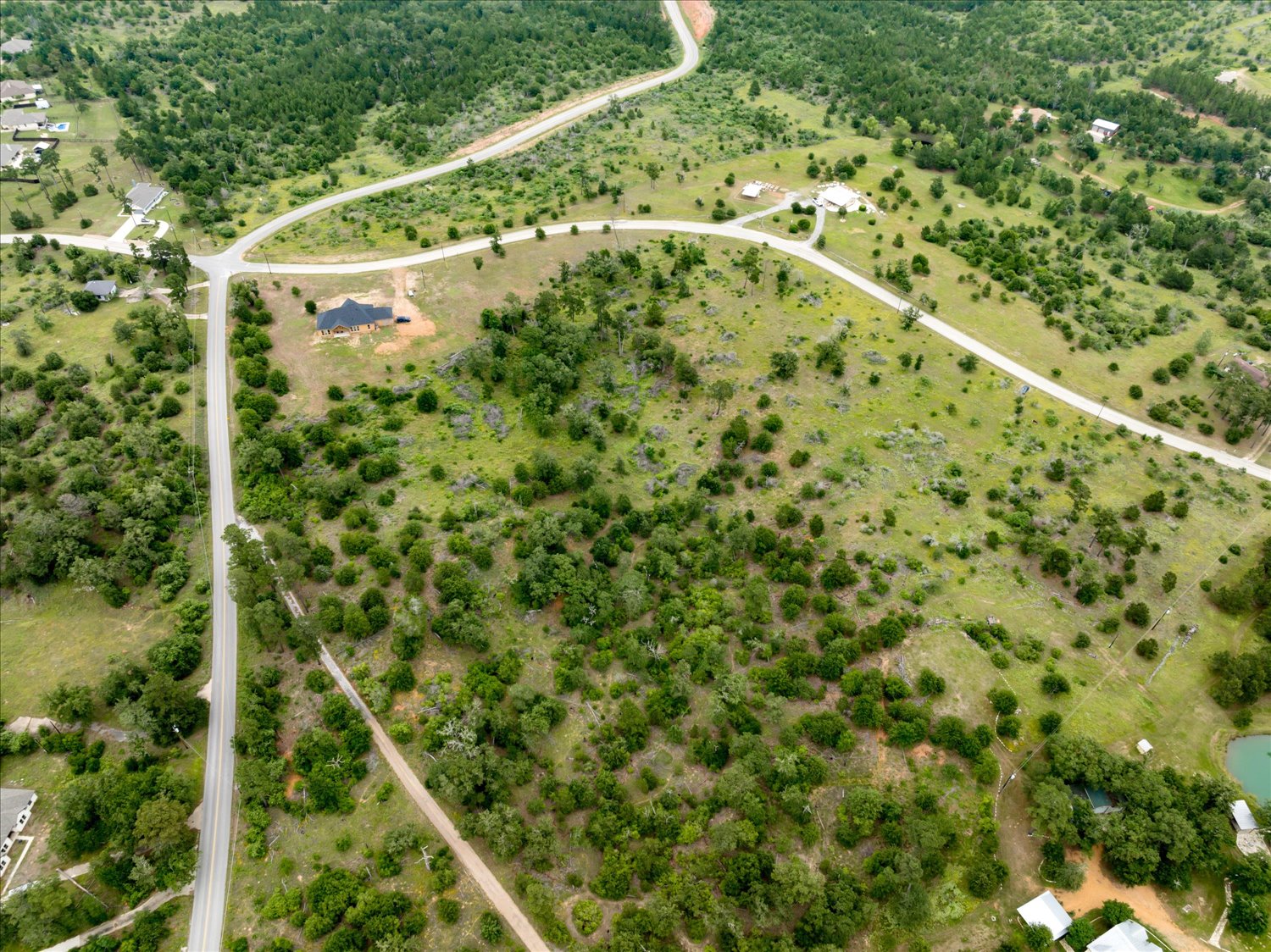 0 McAllister Road Bastrop, TX 78602 - Photo 4 of 12 An aerial perspective reveals a vast, verdant lot intersected by roads and bordered by lush woodlands.