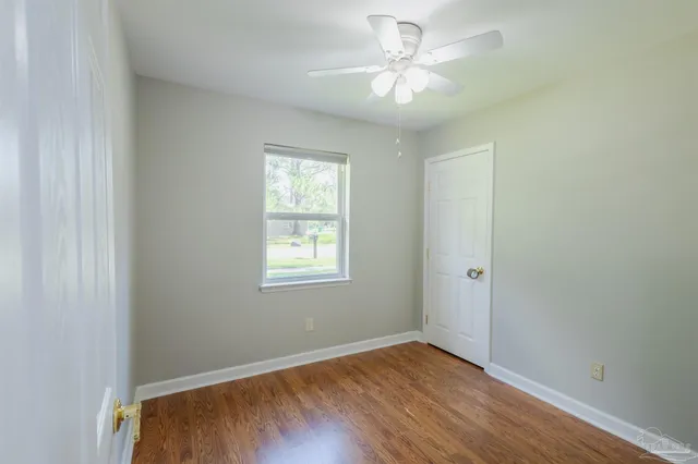 an empty room with wooden floor ceiling fan and window