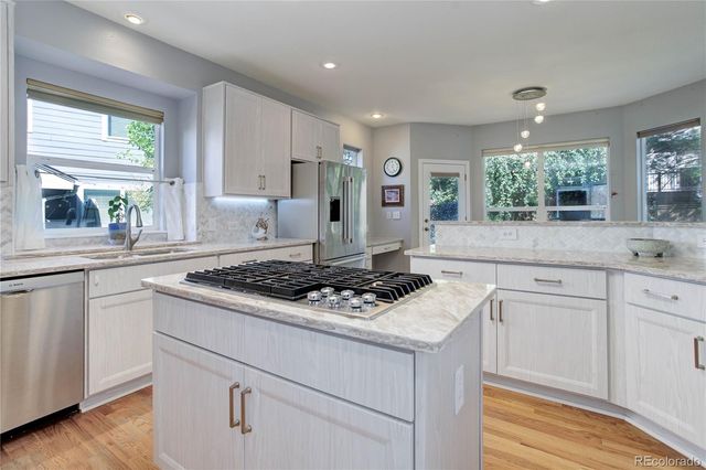 a kitchen with stainless steel appliances granite countertop a stove a sink dishwasher and white cabinets with wooden floor