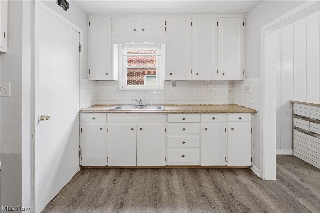 311 Fowles Road Berea, OH 44017 - Photo 9 of 40 Kitchen featuring extensive white cabinetry, a double basin stainless steel sink, light-toned countertops, white subway tile backsplash, and wood-finish flooring