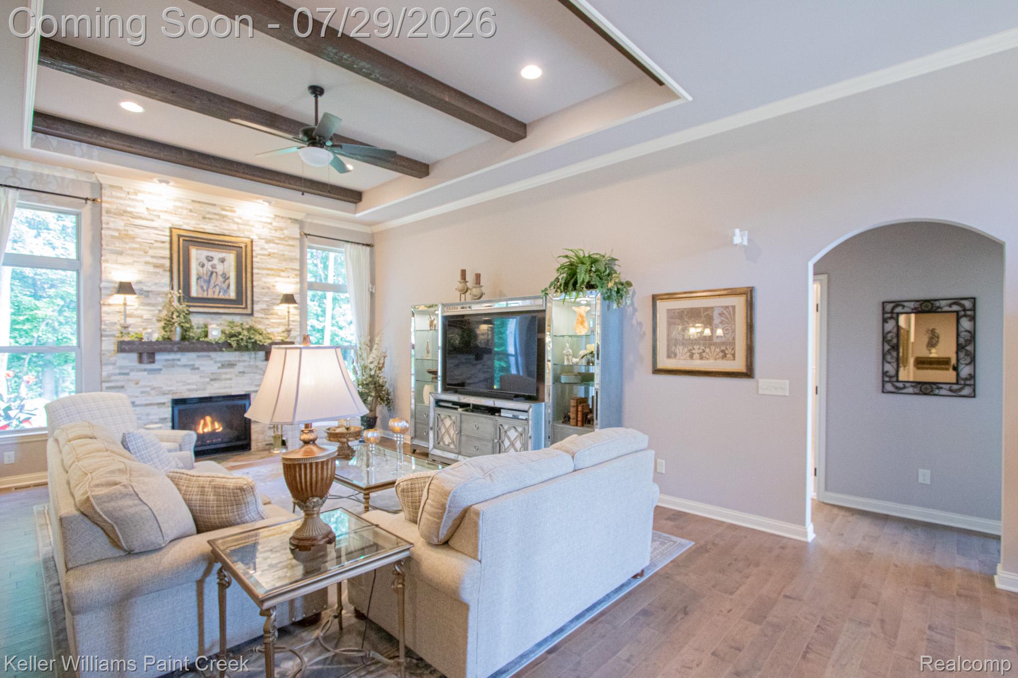Living area featuring a stone-clad fireplace, wood-finish flooring, and a tray ceiling with exposed beams