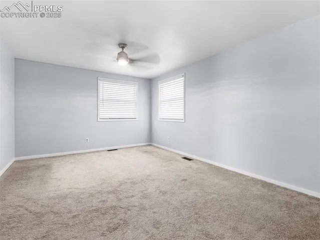 an empty room with a chandelier fan and windows