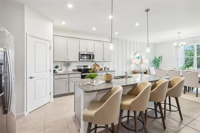 a kitchen with stainless steel appliances kitchen island granite countertop a stove a sink a refrigerator a dining table chairs and white cabinets