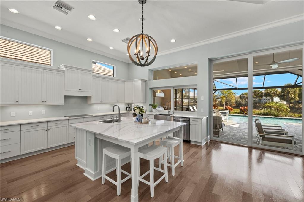 6420 Pembroke Way Naples, FL 34113 - Photo 9 of 39 Kitchen featuring white cabinetry, light quartz counters, black electric cooktop, ornamental molding, and a center island with sink
