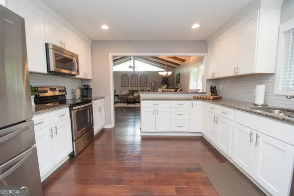 a large kitchen with stainless steel appliances granite countertop a stove top oven a sink a refrigerator and white cabinets with wooden floor