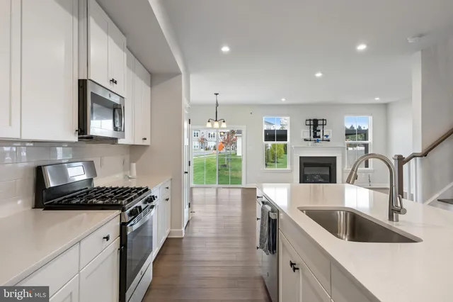 a kitchen with stainless steel appliances kitchen island a stove a sink a microwave a stove and white cabinets with wooden floor