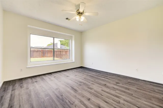 an empty room with wooden floor chandelier fan and windows