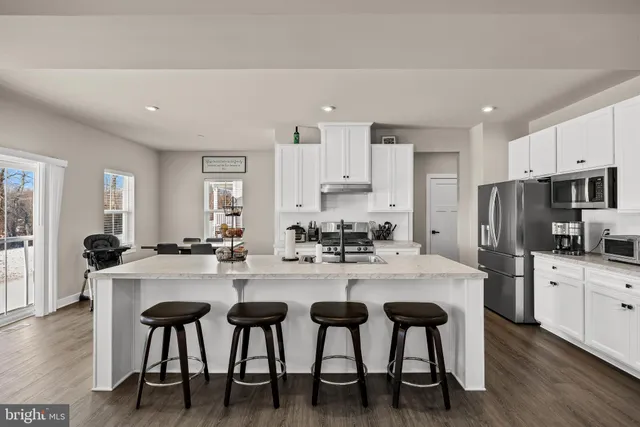 a kitchen with stainless steel appliances kitchen island granite countertop a dining table chairs and refrigerator