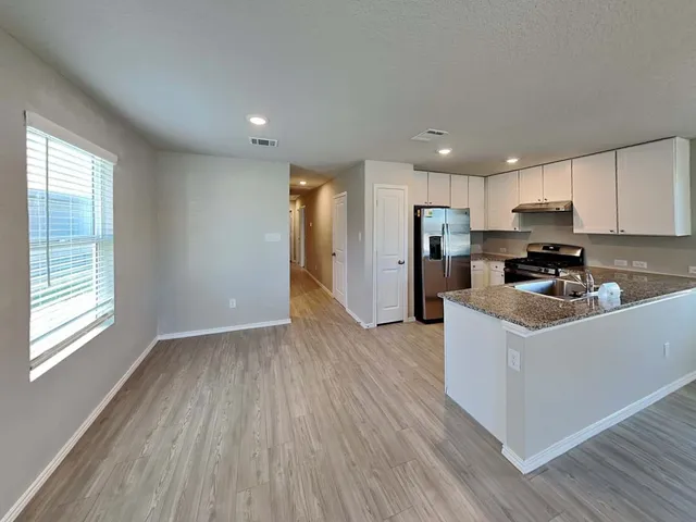 a kitchen with stainless steel appliances granite countertop a refrigerator a stove top oven a sink dishwasher and wooden cabinets with wooden floor