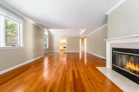 a view of an empty room with wooden floor fireplace and a window