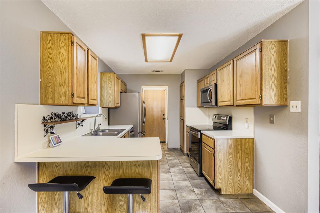 424 Benjamin Lane Arlington, TX 76002 - Photo 9 of 19 Kitchen with appliances with stainless steel finishes, light countertops, a peninsula, a kitchen breakfast bar, and light tile patterned floors