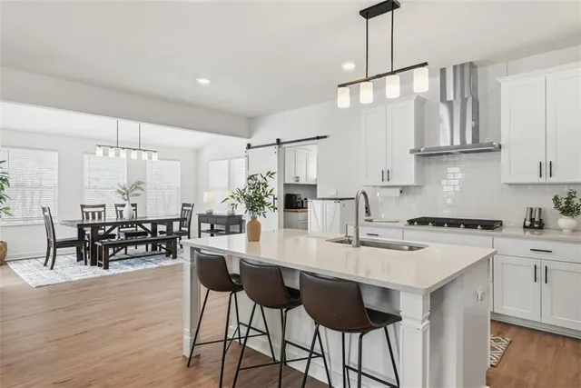 a kitchen with stainless steel appliances kitchen island granite countertop a dining table chairs stove and white cabinets