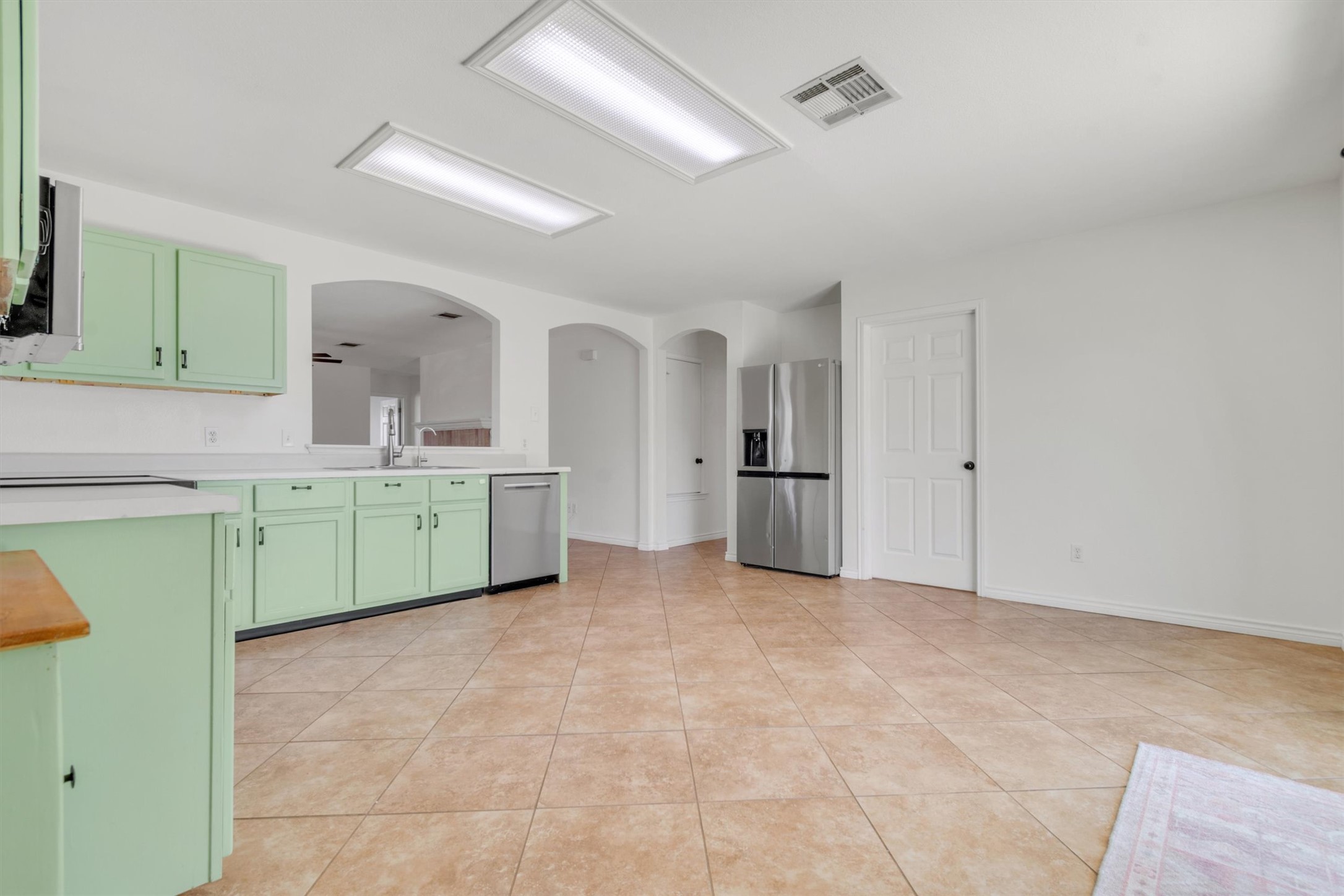 100 Madisons Way Buda, TX 78610 - Photo 12 of 30 Kitchen featuring arched walkways, green cabinets, light countertops, stainless steel appliances, and light tile patterned floors