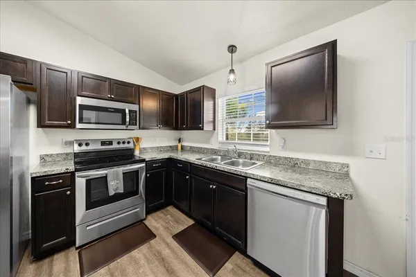 a kitchen with stainless steel appliances granite countertop a stove top oven a sink a dining table and chairs with wooden floor